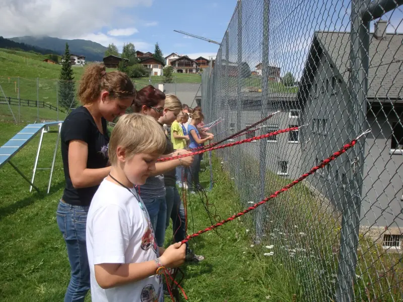 Eine Gruppe von Menschen, die um einen Zaun stehen, mit einer Frau und einem Jungen, die ein Seil halten. – Jugend und Hund Lager 2012 in Vignogn