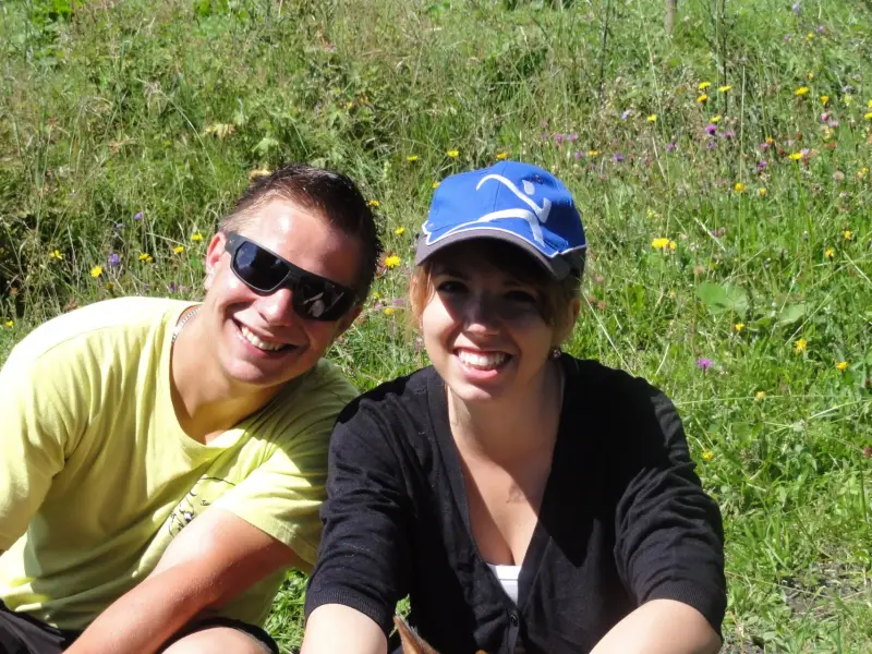 Zwei Frauen, die in einem Feld von Wildblumen nebeneinander sitzen, beide lächelnd. – Jugend und Hund Lager 2012 in Vignogn