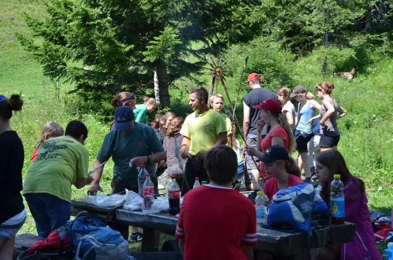Eine Gruppe von Menschen, die um einen Picknicktisch im Wald stehen. – Jugend und Hund Lager 2012 in Vignogn