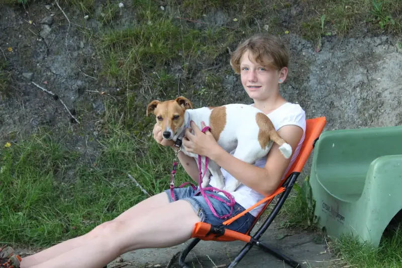 Eine Frau, die auf einem Stuhl mit einem Lächeln auf dem Gesicht sitzt und einen kleinen… Rassen: Italienisches Windspiel, Toy Terrier. – Jugend und Hund Lager 2012 in Vignogn