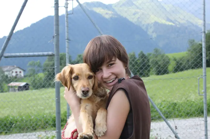 Eine Frau, die mit einem Lächeln auf dem Gesicht einen Hund in den Armen hält. Rasse: Golden Retriever. – Jugend und Hund Lager 2012 in Vignogn